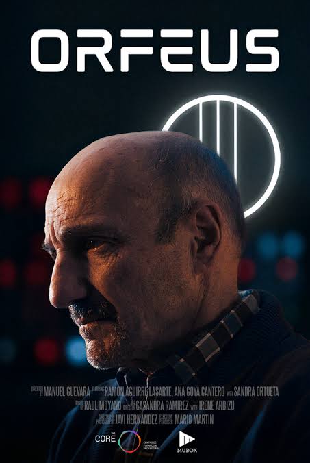 An older bald man in profile, with a lit neon circle behind him.