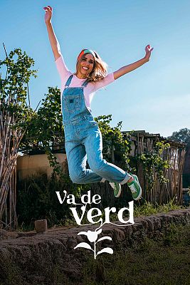 A woman in dungarees jumping in a vegetable garden.